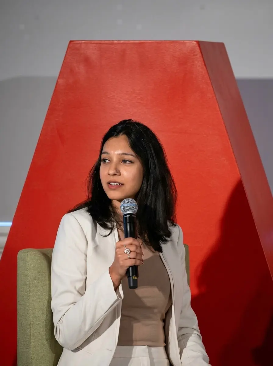 Rhea, in a cream blazer, speaks into a microphone while seated on stage in front of a large red AARP letter A