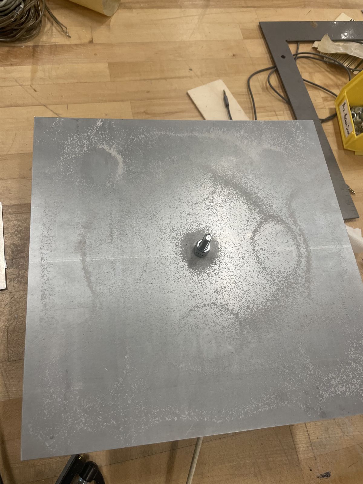 The bare metal plate in the workshop, with faint rings left by the first sand tests