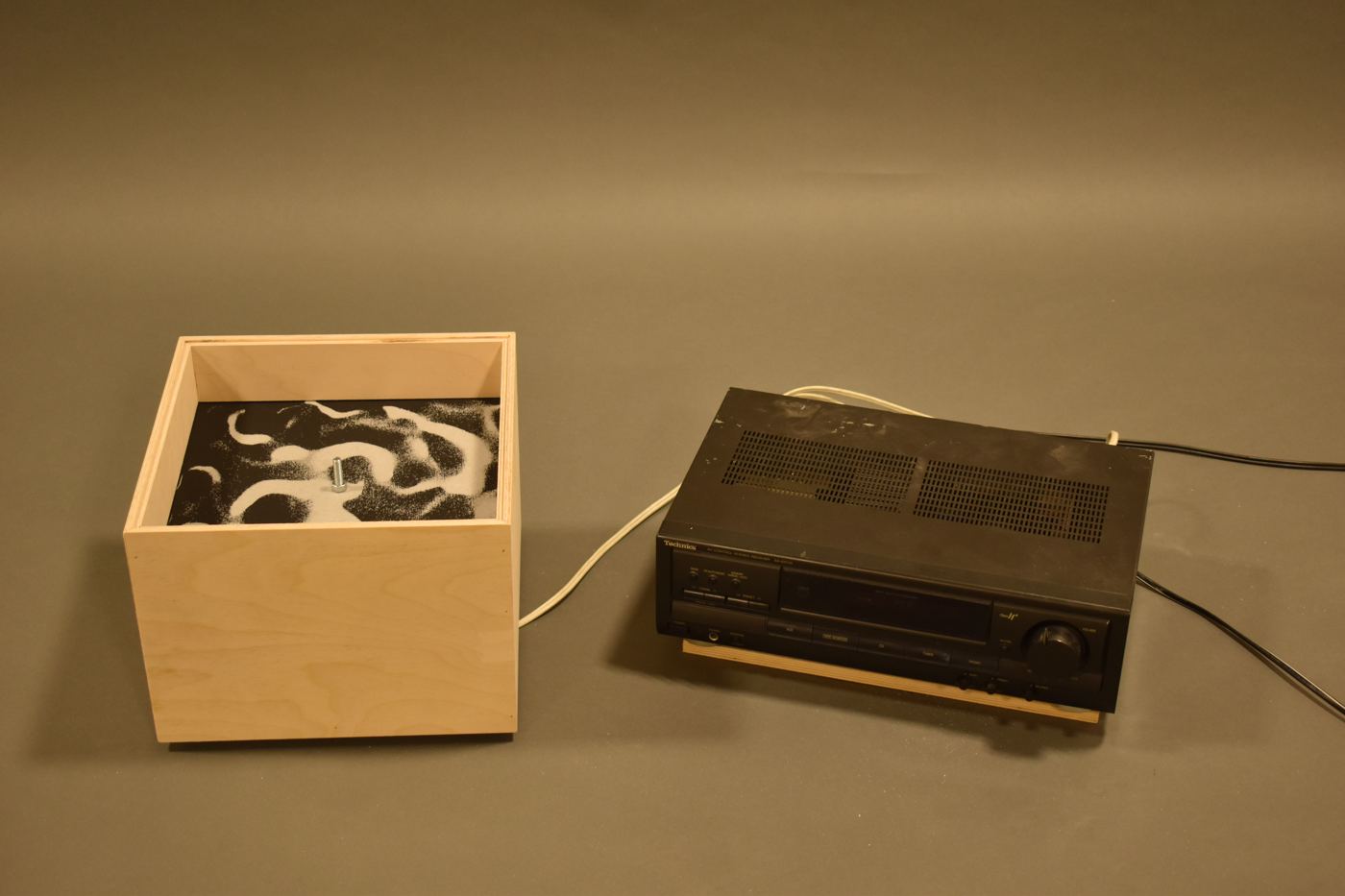 The finished piece: a wooden box of patterned sand beside the amplifier that drives it